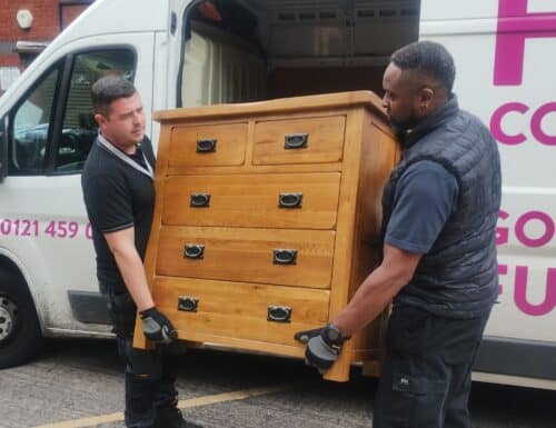 Two men carrying a set of wooden drawers from a van.