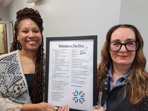 Two women holding a picture frame which contained a poem about Birmingham Hospice cafe The Hive.
