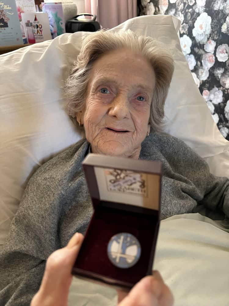 A elderly woman lying in her bed holding a special brooch.